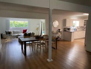 Relax in a spacious living area with a dining table and chairs, surrounded by a large window offering a view of lush greenery.