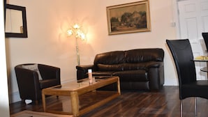 Ein Wohnzimmer mit braunem Ledersofa, einem Glastisch, einem schwarzen Sessel und einem Bild an der Wand.