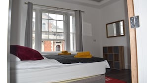 Ein Schlafzimmer mit Bett, einem Fenster mit Vorhängen, einem Spiegel und einem Holzschrank.
