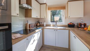 Una cocina moderna con armarios blancos, una campana extractora de acero inoxidable, un horno empotrado, un ventanal con persianas y una encimera con diversos utensilios de cocina.
