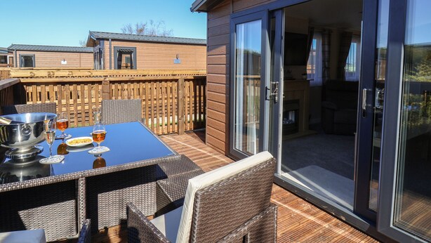 Terraza de madera con mesa lista para comer, una parrilla y un porche acristalado con puerta corrediza.