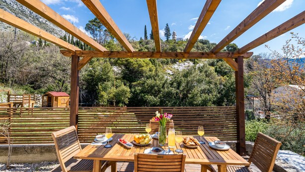 A wooden pergola with a table set for a meal, surrounded by natural scenery. - Apartment Koko - Two Bedroom with Terrace (Dubrovnik)