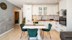 A modern kitchen with white cabinets, a central island, and a dining area with green chairs. - Apartment Koko - Two Bedroom with Terrace (Dubrovnik)