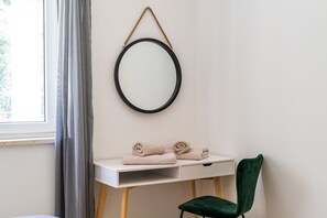 Um quarto com uma escrivaninha branca, uma cadeira verde e um espelho redondo na parede.