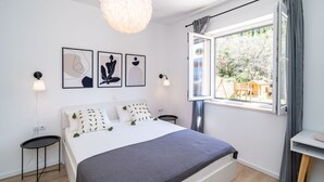 A modern bedroom with a large bed, a hanging light fixture, and a window with curtains. - Apartment Koko - Two Bedroom with Terrace (Dubrovnik)