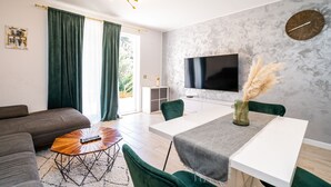 A modern living room with a sofa, a coffee table, a dining table with chairs, a TV, and a decorative vase. - Apartment Koko - Two Bedroom with Terrace (Dubrovnik)