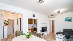 A modern living room with a dining table, sofa, TV, and kitchen in the background. - Apartment N&I - One Bedroom with Terrace (Dubrovnik)