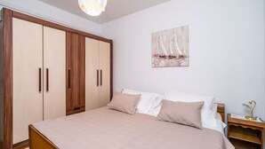 A bedroom with a bed, wooden wardrobe, and a painting of sailboats on the wall. - Apartment N&I - One Bedroom with Terrace (Dubrovnik)