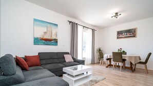 A modern living room with a grey sofa, a white coffee table, and a dining area with a table and chairs. - Apartment N&I - One Bedroom with Terrace (Dubrovnik)