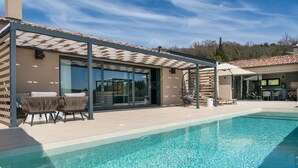 Un espace piscine extérieur moderne, doté d’une pergola, de sièges et offrant une vue dégagée sur la piscine.