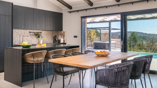 Une cuisine moderne avec des meubles de couleur sombre, un îlot central en bois et un coin repas doté de chaises en osier.