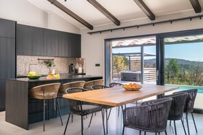 Una cocina moderna con armarios oscuros, una isla de madera y un comedor con sillas de mimbre.
