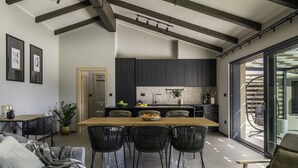 Une cuisine moderne avec des meubles de rangement sombres, une table à manger en bois et une grande fenêtre.