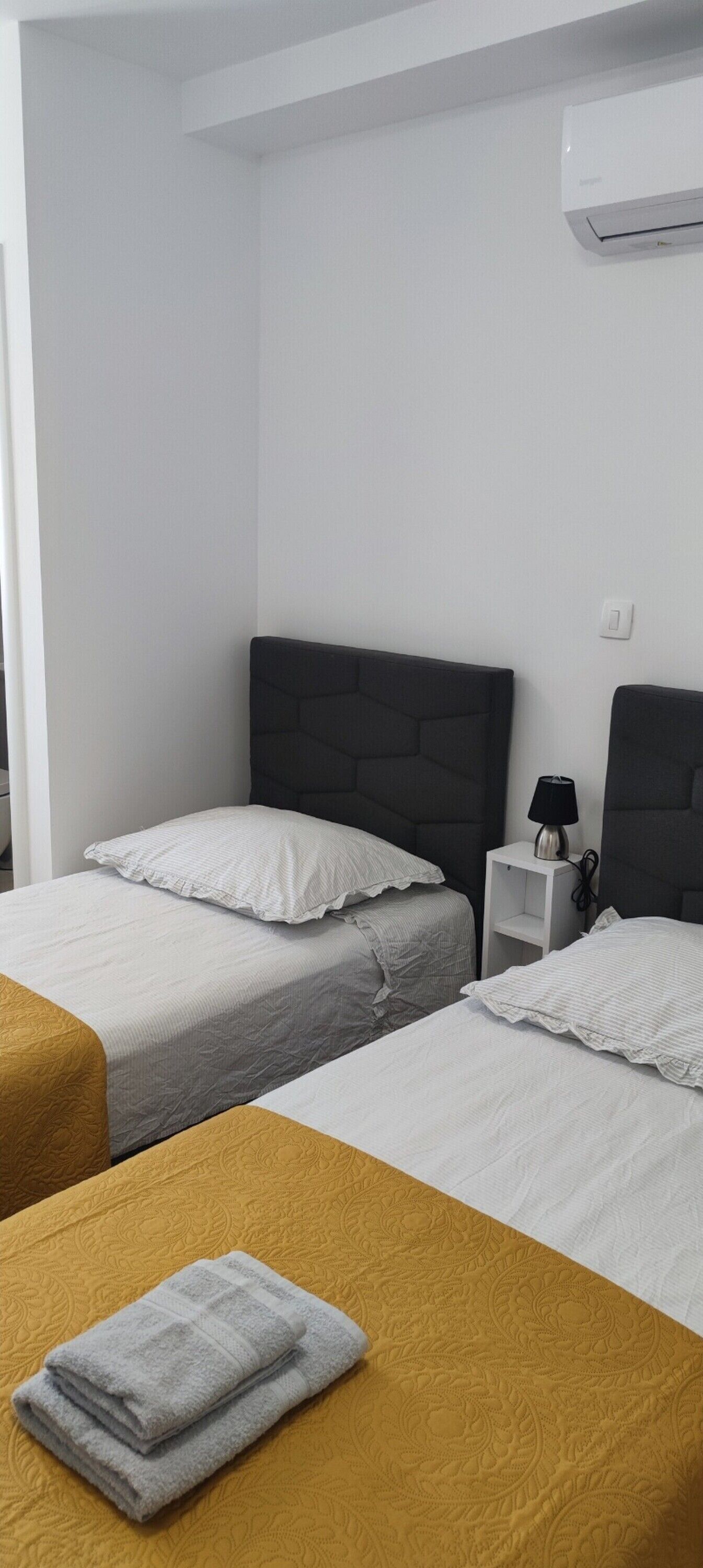 A hotel room with two beds, a nightstand, and an air conditioning unit.