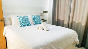 Siisti hotellihuone, jossa on huolitellusti pedattu sänky, kaksi koristeellista tyynyä, siististi taitettu pyyhe, yöpöytä ja verho.
