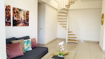 Una sala de estar moderna con un sofá gris, cojines coloridos, una escalera espiral y dos cuadros abstractos en la pared.