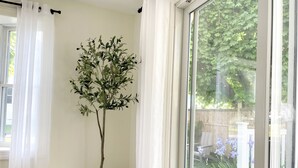 A room with a large window, a white curtain, and a tall plant in a woven pot. - Coastal Chic Home on the Island of Cape May  (Cape May)