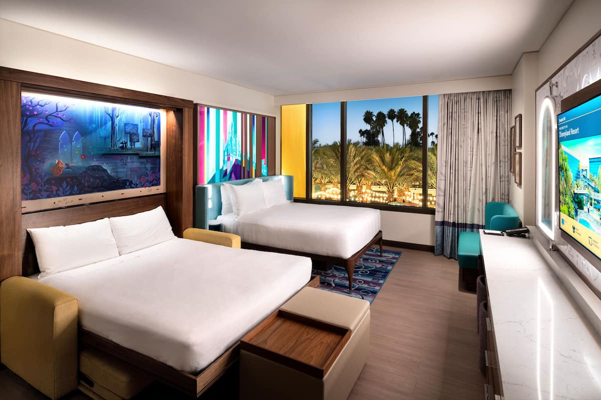Ein Hotelzimmer mit zwei Betten, einem Fernseher, einem großen Fenster mit Blick auf Palmen und einem Bild an der Wand.