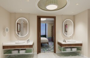 A hotel bathroom with two sinks, mirrors, and a bed visible through an archway.