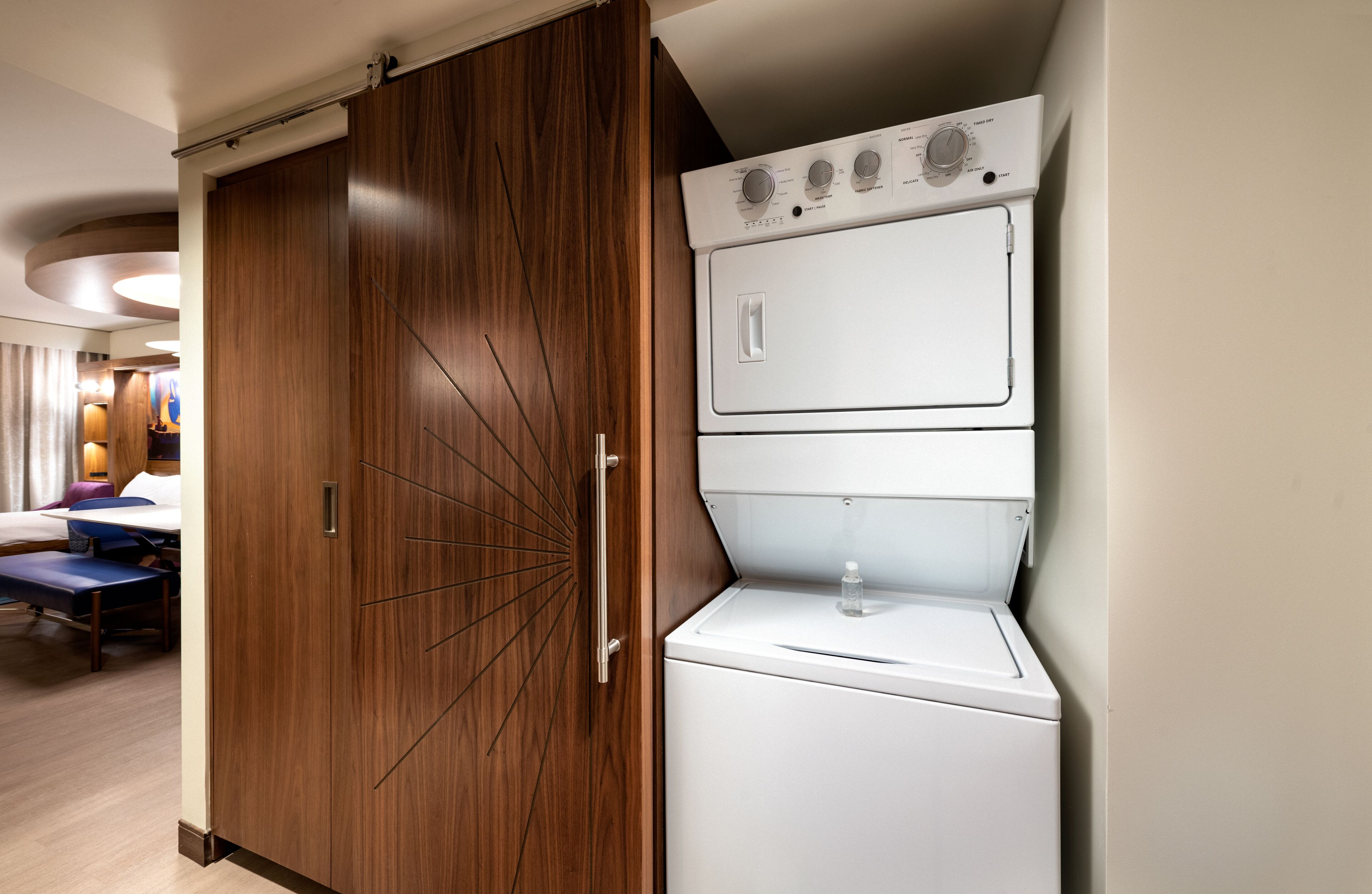 A hotel room with a wooden wardrobe, a washing machine, and a bed with a blue headboard.