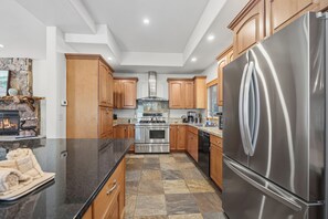 Una cocina moderna con refrigerador de acero inoxidable, encimeras de granito, gabinetes de madera y chimenea de piedra.