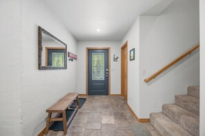 A hallway with a bench, a door with a glass panel, a wooden staircase, and a wall-mounted mirror.