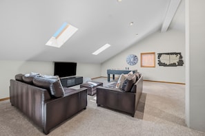 A spacious living room with a high ceiling, a flat-screen TV, and a foosball table.