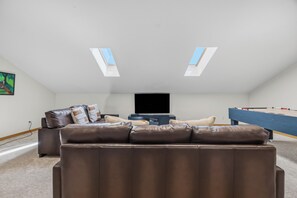 Una sala de estar moderna con un sofá de cuero marrón, un televisor de pantalla plana y una mesa de billar.