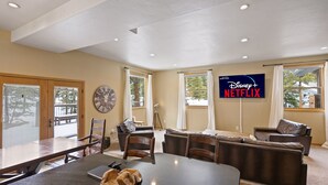 Amplia sala de estar con una mesa oscura grande, sofás de cuero y un televisor con el logotipo de Disney+ Netflix.