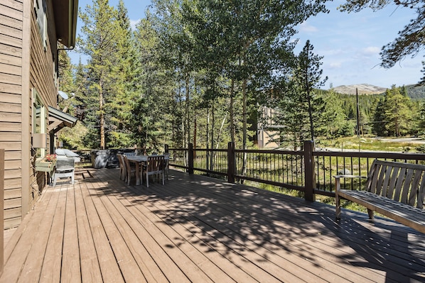 A wooden deck with a table and chairs, surrounded by a wooden fence and trees.