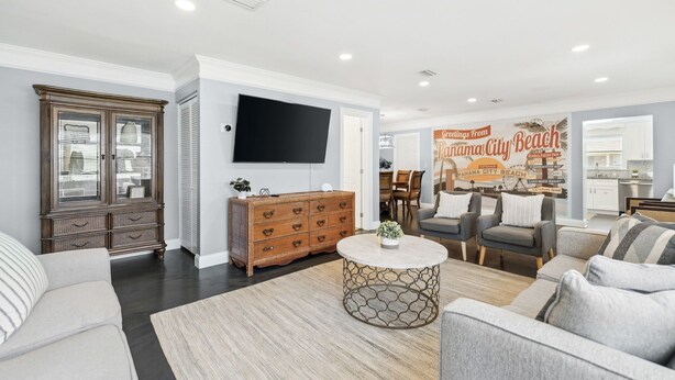 A spacious living room with a large flat-screen TV, a wooden cabinet, a round coffee table, and a seating area with two armchairs and a sofa. - Steps to Beach! |Sleeps 11!| Summer Ready! (Panama City)