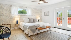A bedroom with a bed, a ceiling fan, a window with curtains, a nightstand, a chair, and a view of the outside. - Steps to Beach! |Sleeps 11!| Summer Ready! (Panama City)