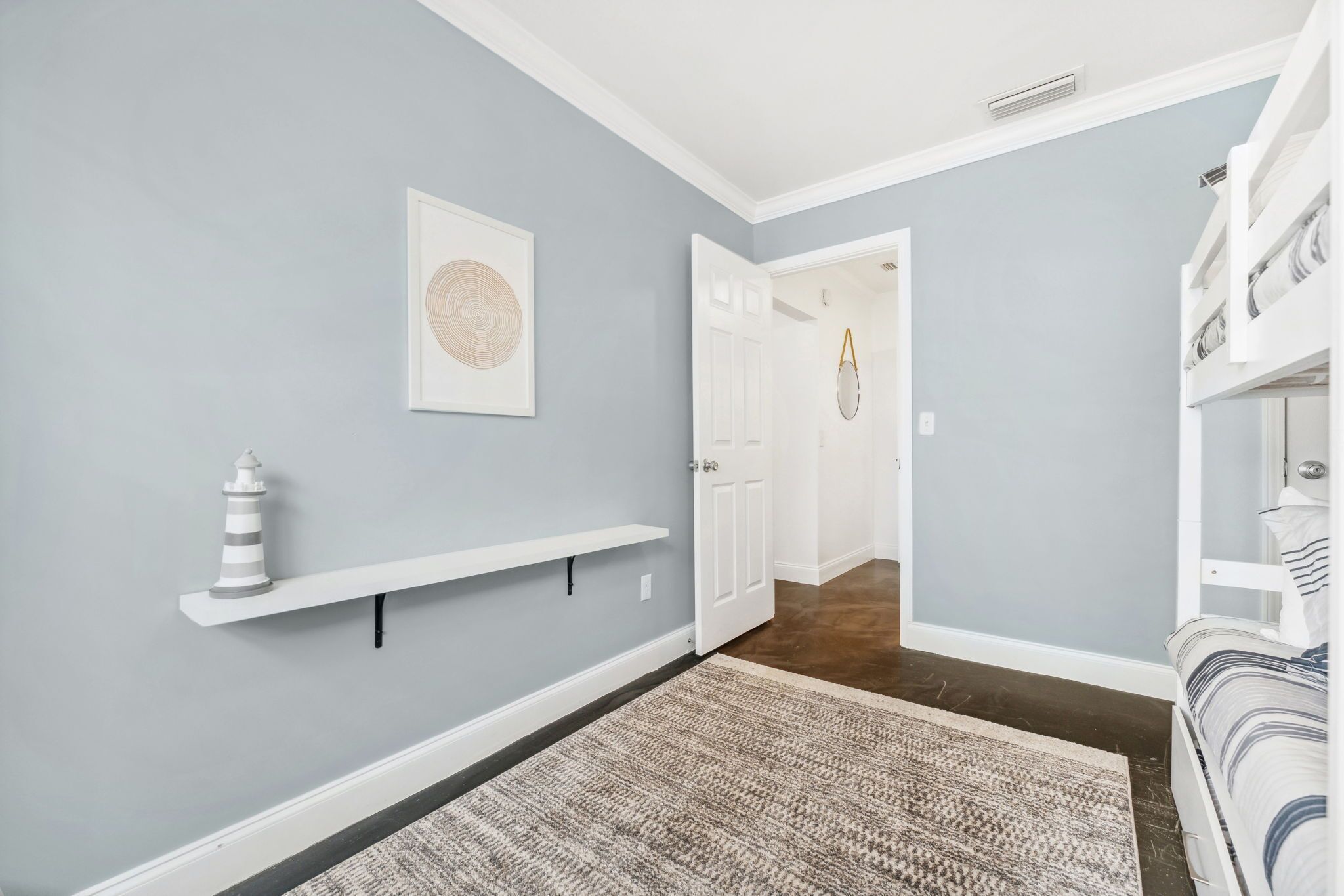 A hallway with a light blue wall, a white door, a white shelf with a decorative item, and a patterned rug.