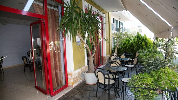Un espace extérieur aménagé avec des tables et des chaises, un arbre en pot et l’entrée d’un bâtiment dotée d’un cadre rouge et de portes en verre.