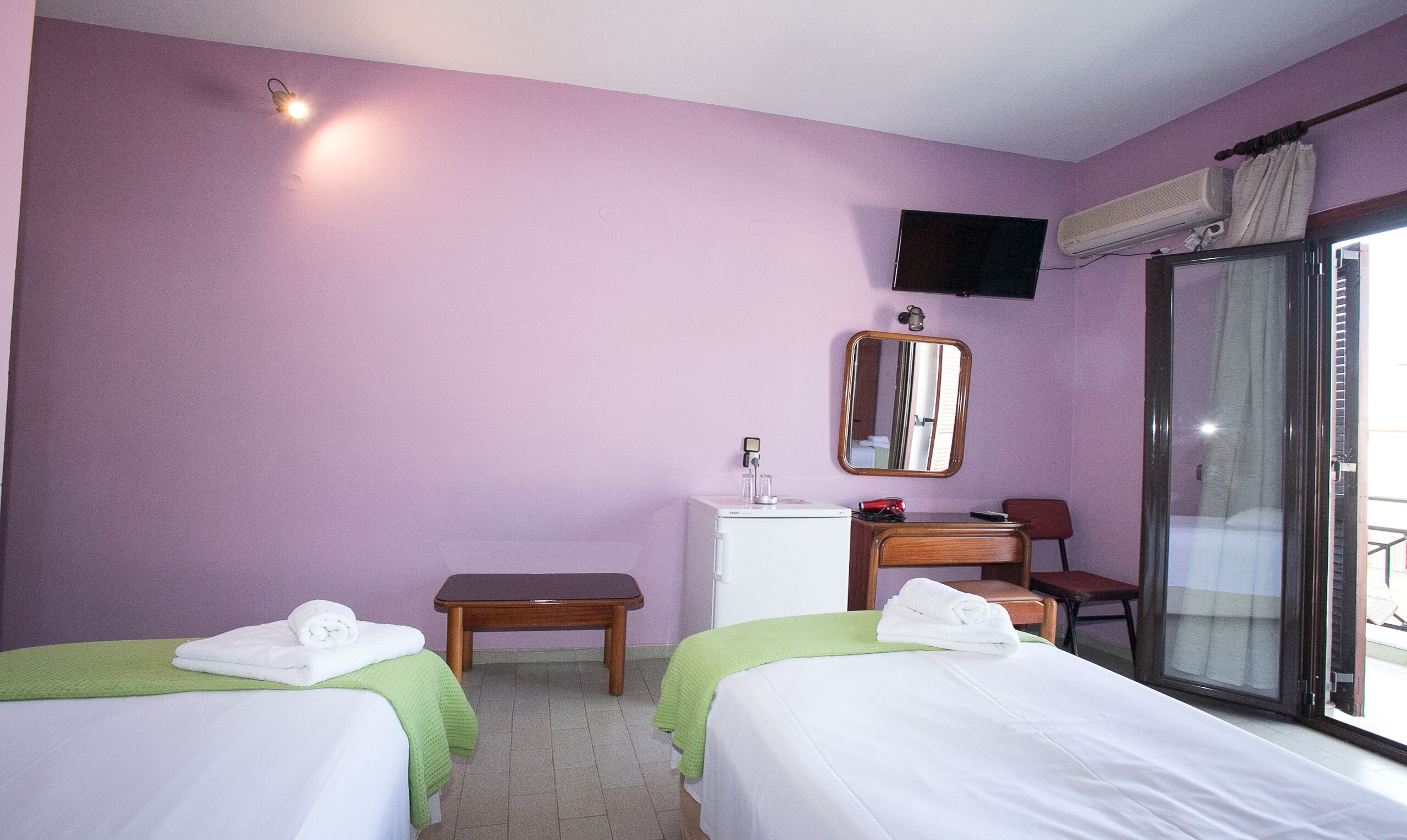 A hotel room with two beds, a desk, a chair, a mirror, and a TV.