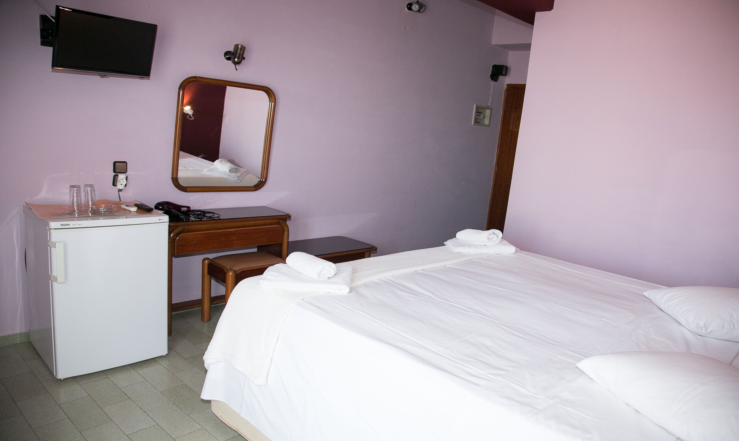 Habitación de hotel con cama, escritorio, espejo, secador de pelo y refrigerador pequeño.