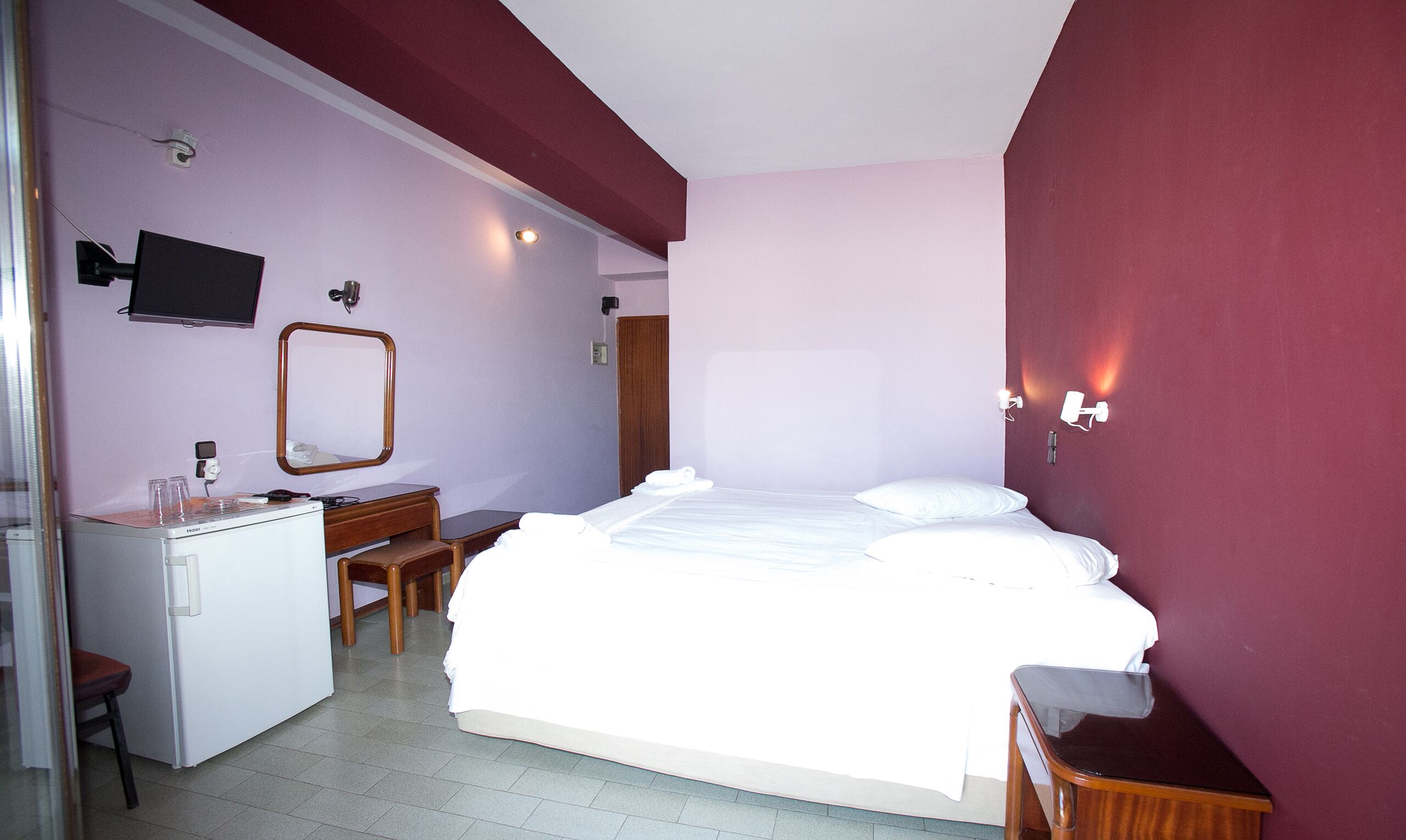 Habitación de hotel con cama, escritorio, silla, espejo y televisor.