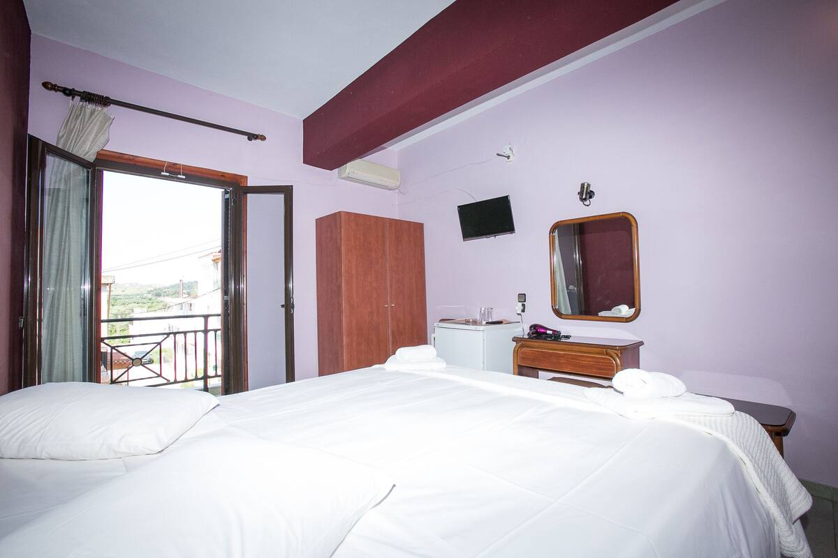 Une chambre d’hôtel avec un lit, une armoire en bois, un petit bureau avec un miroir et un téléviseur fixé au mur.