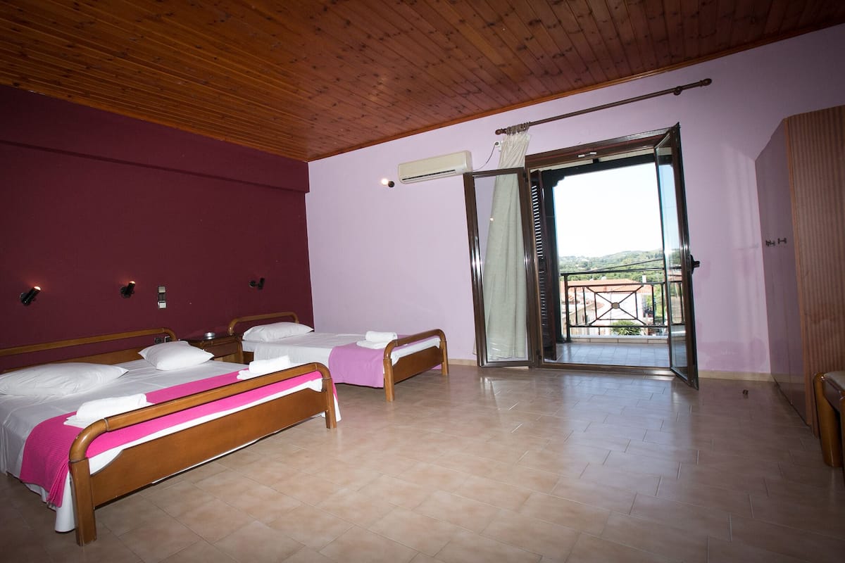 Une chambre avec deux lits, un plafond en bois, une porte-fenêtre coulissante donnant sur un balcon et un appareil de climatisation fixé au mur.