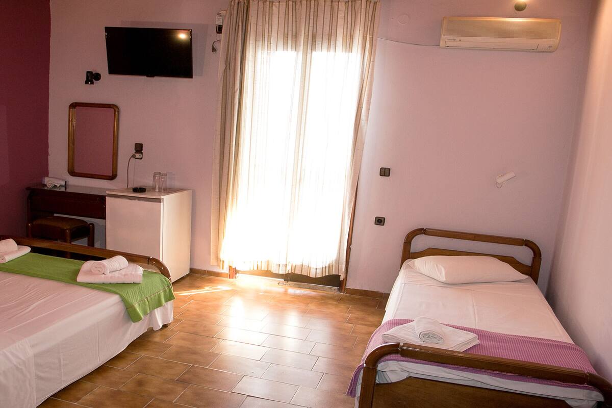 Une chambre d’hôtel avec deux lits, un bureau, une télévision et une fenêtre avec des rideaux.