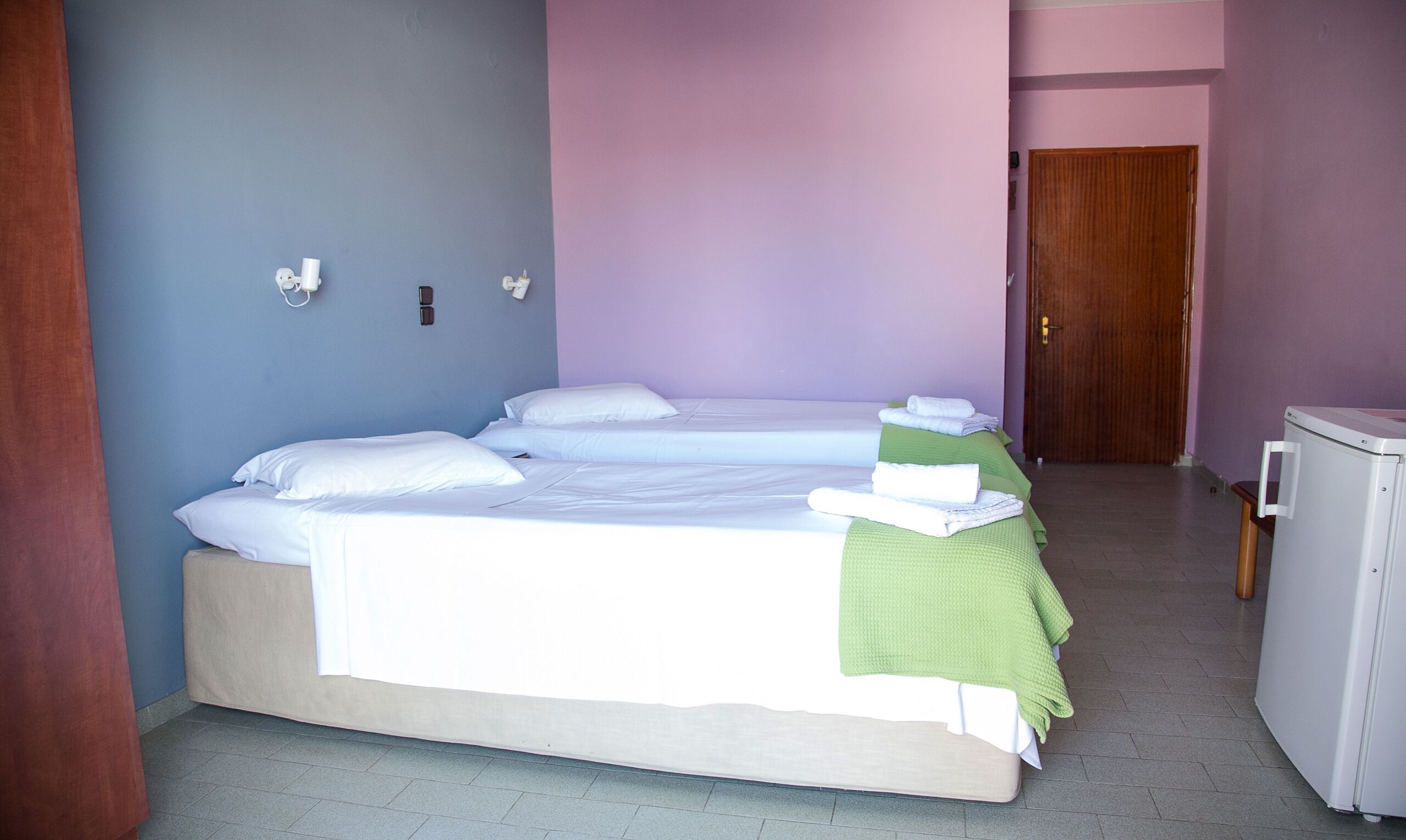 A hotel room with two beds, a small refrigerator, and a wooden door.