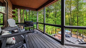 Una terraza techada con una parrilla, asientos y vista a un bosque.