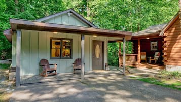 Relax on the porch with two Adirondack chairs, surrounded by lush greenery.