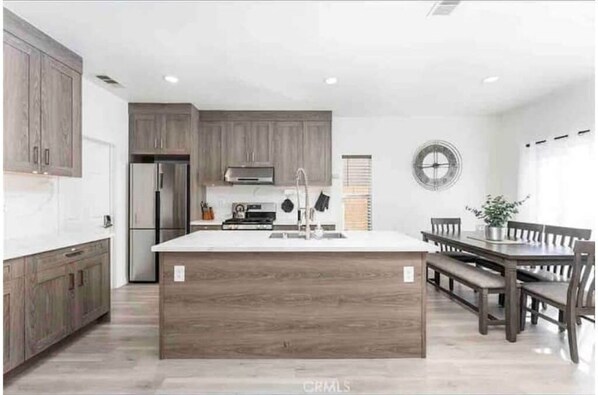 Enjoy cooking in the well-equipped kitchen with a central island, sink, and range hood, adjacent to a dining area with a wooden table and benches.