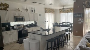 Een moderne keuken met witte kasten, een centraal eiland met krukken en een zithoek met een bank en stoelen.