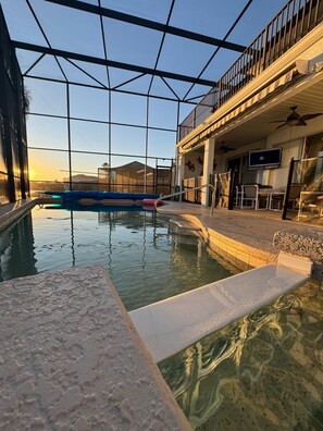 Piscina interior com paredes de vidro transparente, área de estar à beira da piscina e varanda com vista para a piscina.