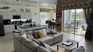 Een moderne woonkamer met een grijze bank, een salontafel, en een keuken met witte kasten en een zwart aanrecht.