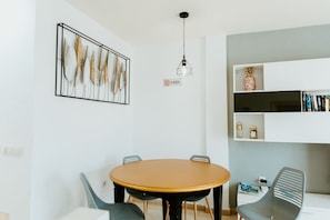 Un comedor con una mesa redonda, sillas, una lámpara colgante, un estante empotrado con libros y objetos decorativos, y una obra de arte enmarcada.