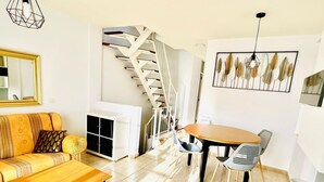 A living room with a sofa, a dining table with chairs, a staircase, and a wall-mounted artwork. - Spacious 2 Bedroom Golden Apartment (Callao Salvaje)