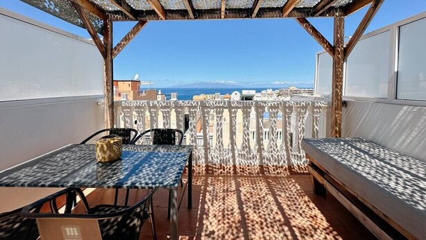 A balcony with a table, chairs, and a sofa, overlooking a cityscape and the sea. - Spacious 2 Bedroom Golden Apartment (Callao Salvaje)